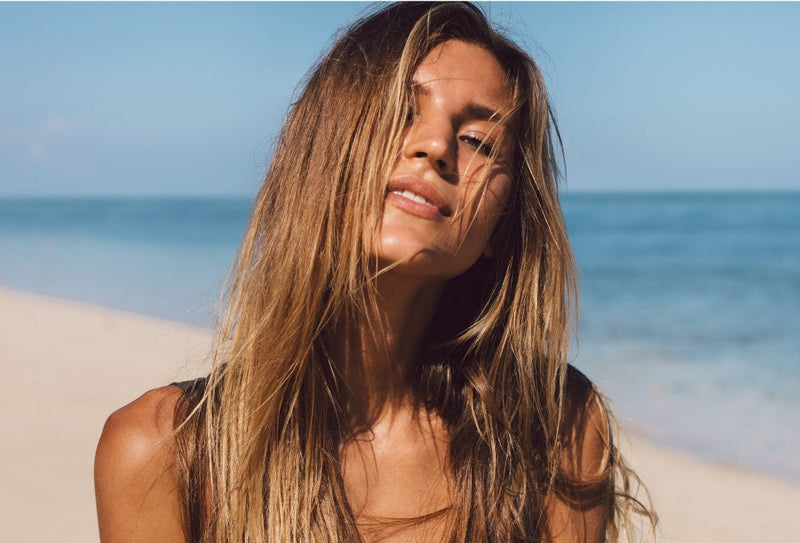 junge Frau mit langen Haaren steht am Strand
